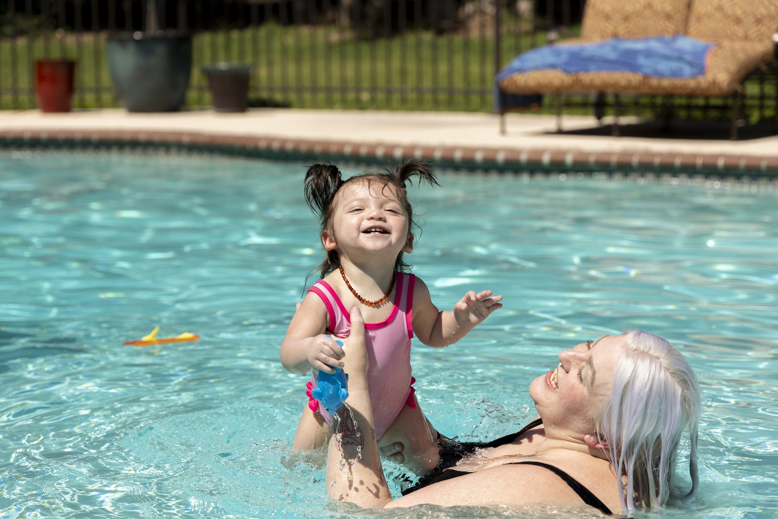 Woman holding up a toddler inside a swimming pool.